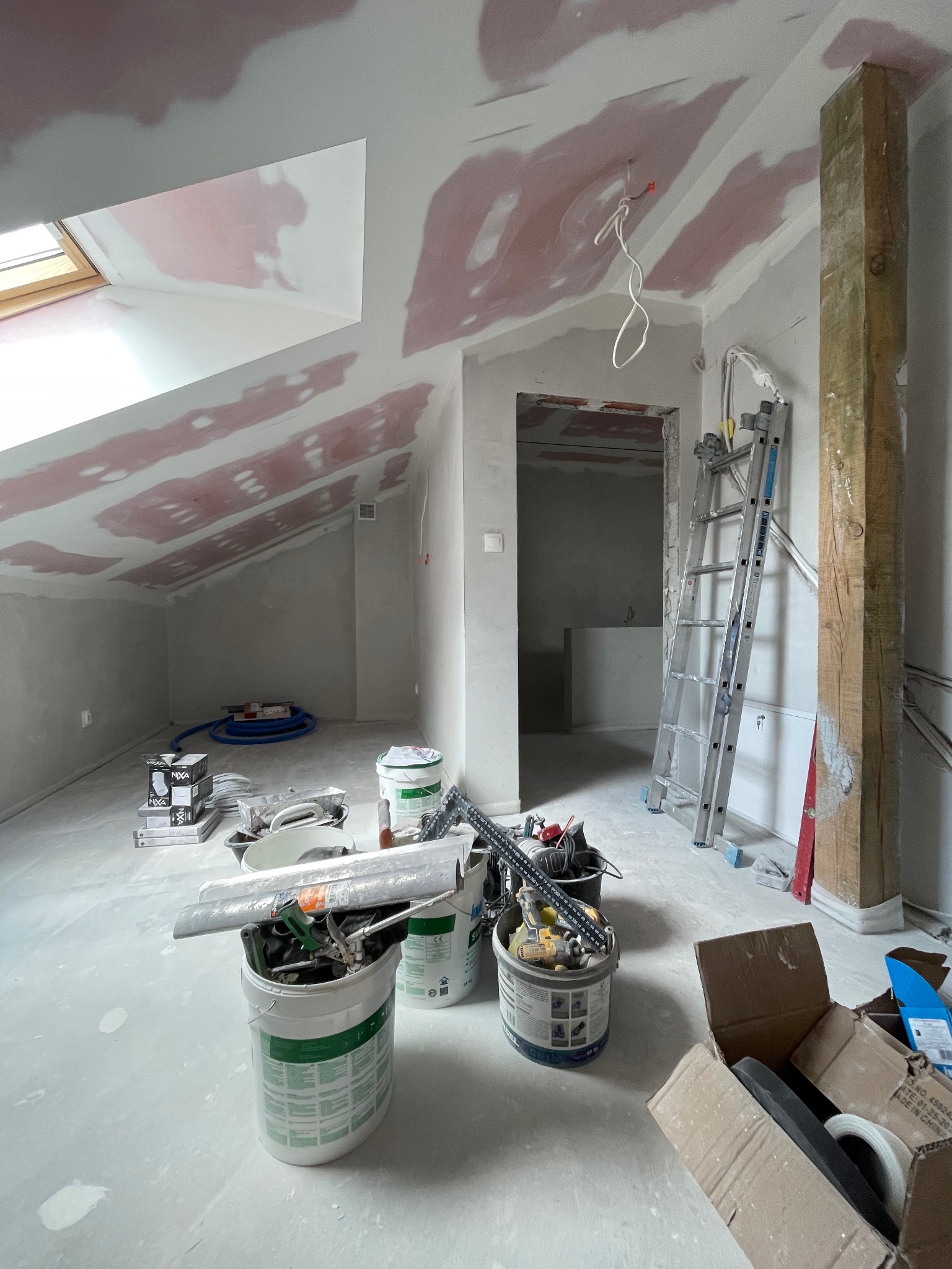 Poddasze w trakcie szpachlowania w Skarżysku-Kamiennej. Widoczne narzędzia, drabina, sufit ze skosami i oknem dachowym, częściowo przygotowany pod malowanie.