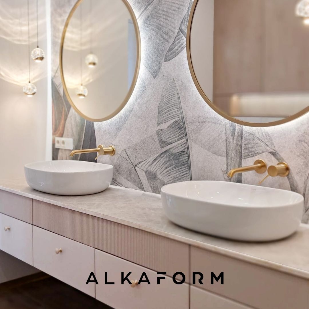 Nowoczesna łazienka z dwiema owalnymi umywalkami nablatowymi, złotymi bateriami i okrągłymi lustrami z podświetleniem LED na tle ściany z motywem liści.