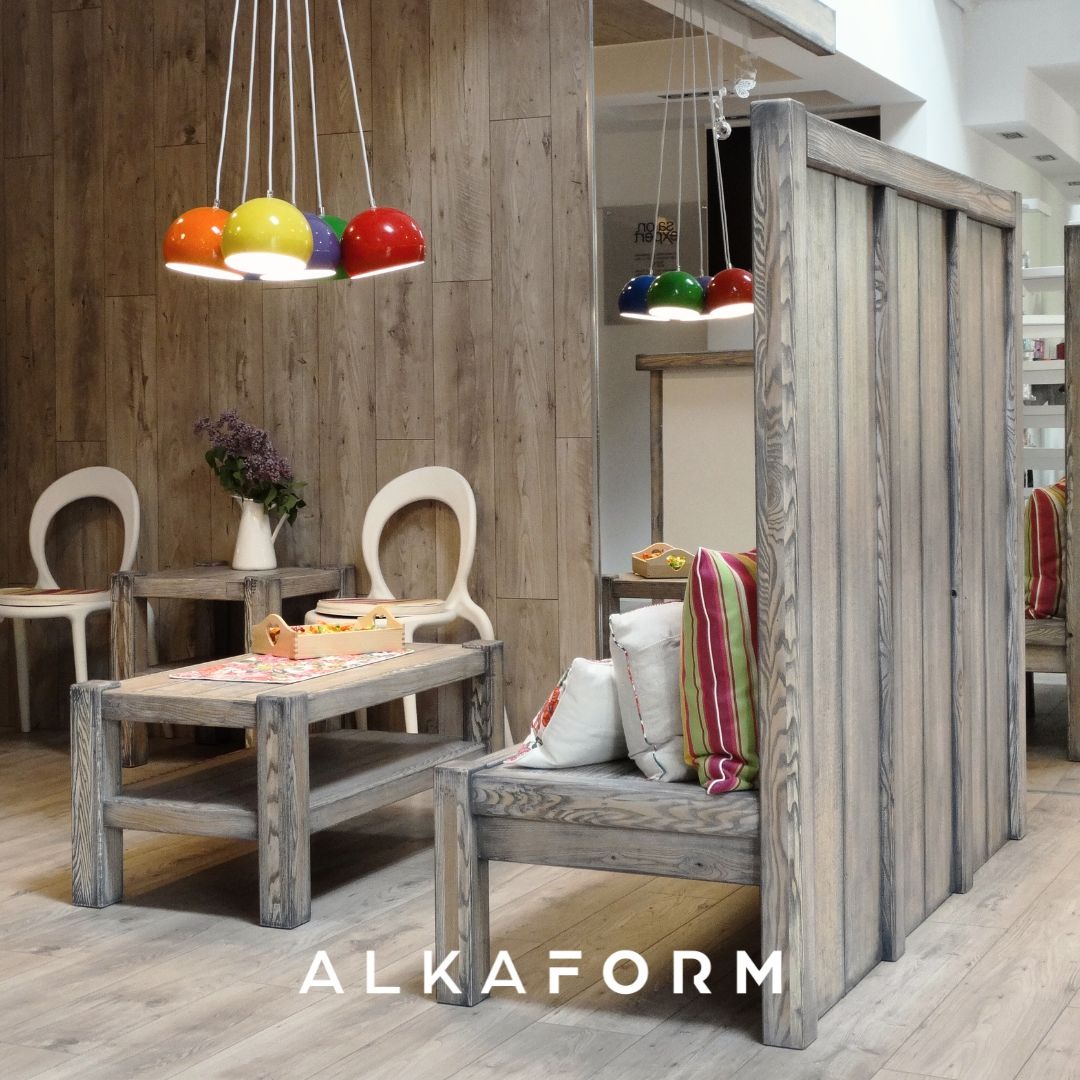 Drewniane meble w salonie z kolorowymi lampami wiszącymi: stolik kawowy, krzesła z wysokim oparciem, sofa z dekoracyjnymi poduszkami i ścianka działowa z pionowych desek.