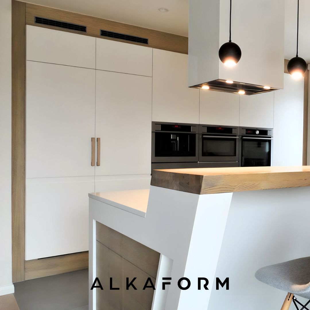 Minimalistyczna kuchnia z białymi frontami szafek, drewnianymi akcentami i wyspą z blatem z jasnego drewna, oświetlona wiszącymi lampami kulami.