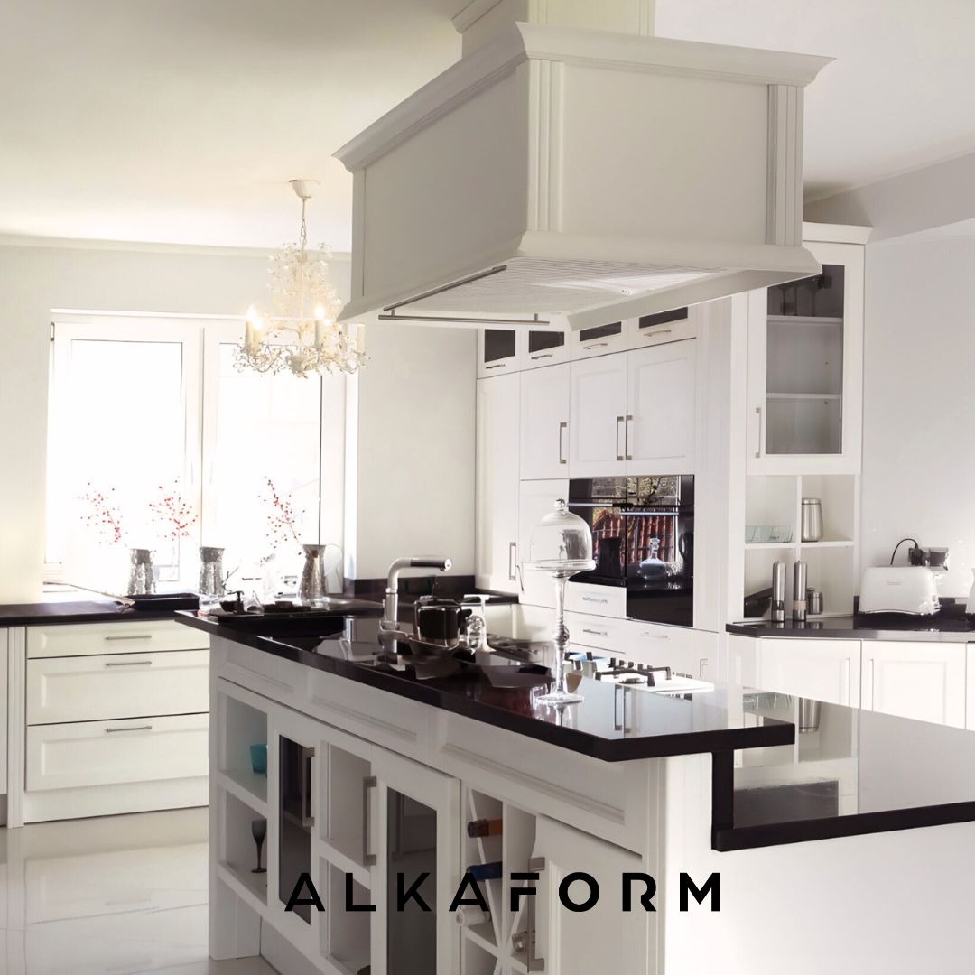 Jasna kuchnia z wyspą i czarnym blatem, nad którą wisi ozdobny okap i żyrandol, widoczne szklane witryny w wyspie i białe fronty szafek.