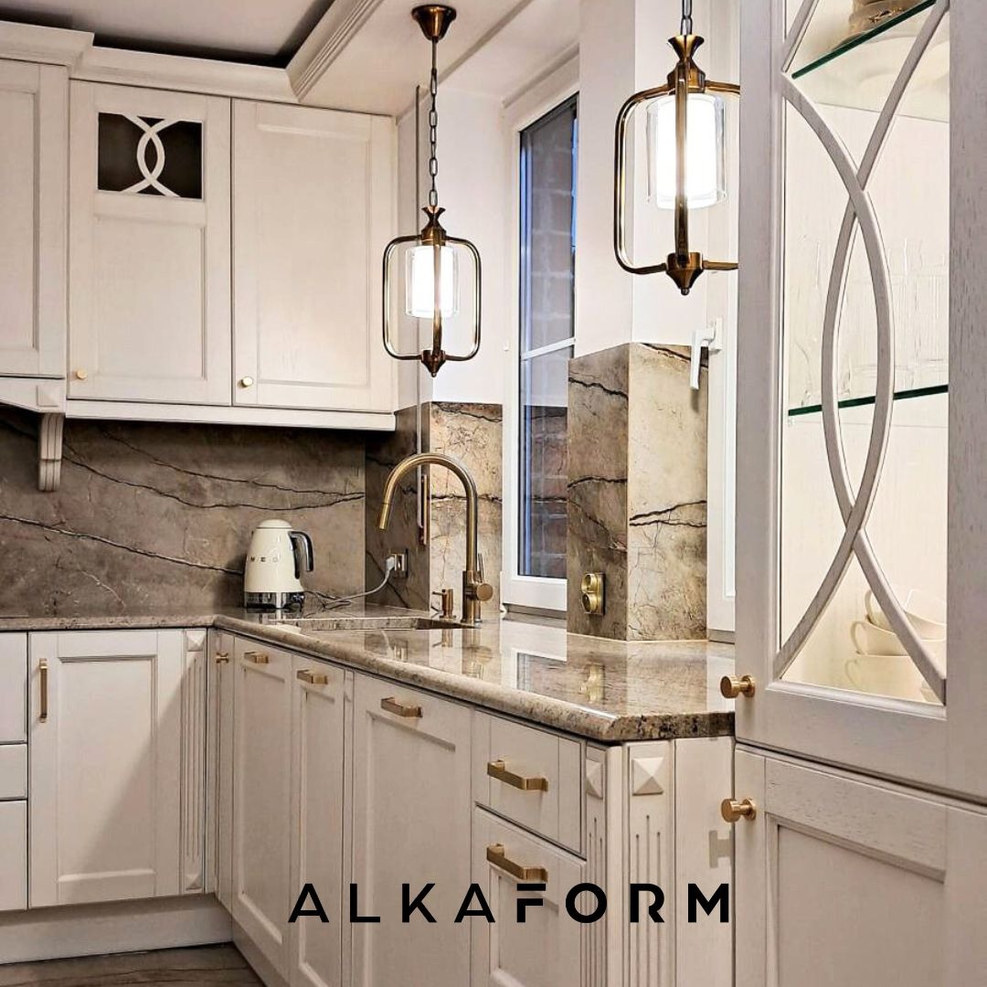 Jasna kuchnia z marmurowym blatem i backsplashiem, oświetlona wiszącymi lampami z metalowymi ramami, z widocznym logo firmy na dolnej szafce.