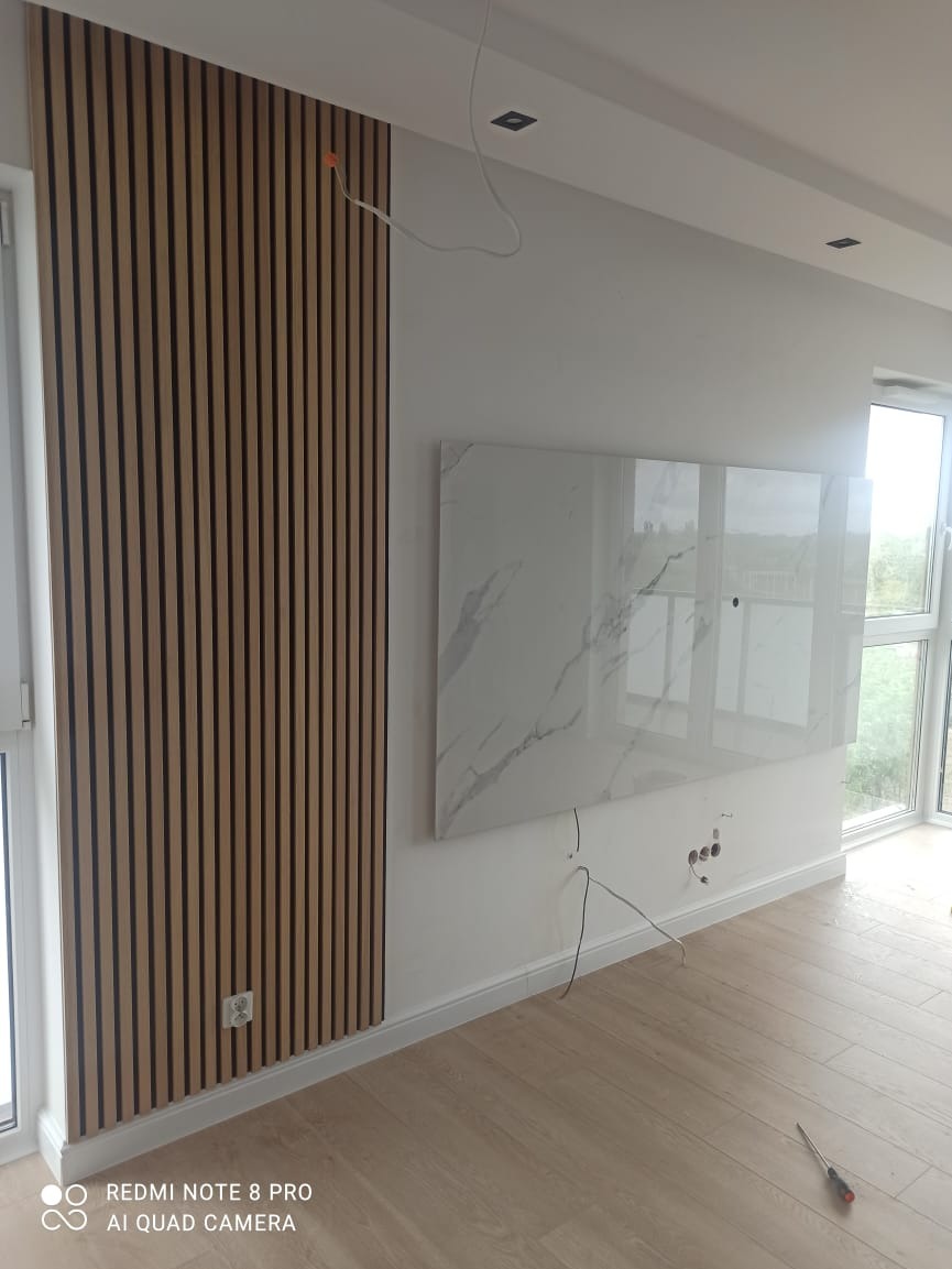 Ściana z drewnianych paneli akustycznych, imitacja marmuru na ścianie, widoczne kable i gniazdka elektryczne, podłoga z paneli.