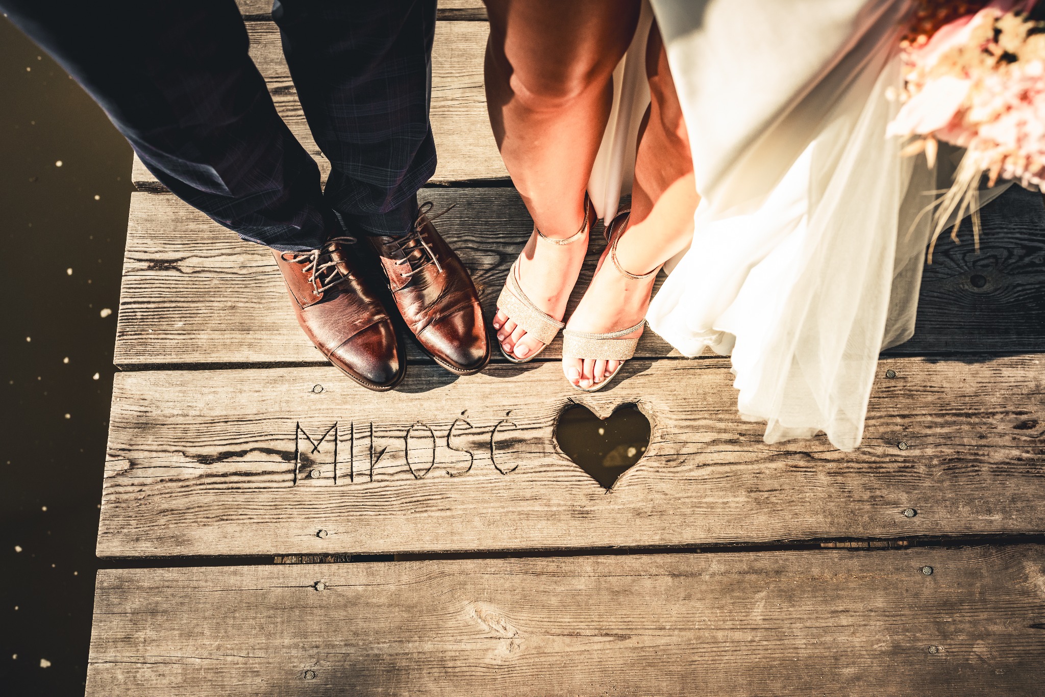 Buty pana młodego i panny młodej stojące na drewnianym pomoście z wyrytym napisem 'Miłość' i sercem.