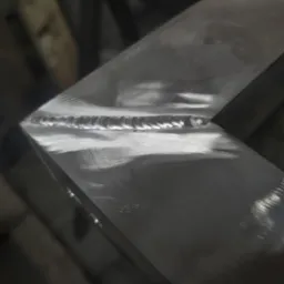 Szczegółowe zbliżenie na spawany narożnik metalowej konstrukcji. Widoczny równy, estetyczny spaw na szlifowanej powierzchni. Precyzyjne łączenie elementów.