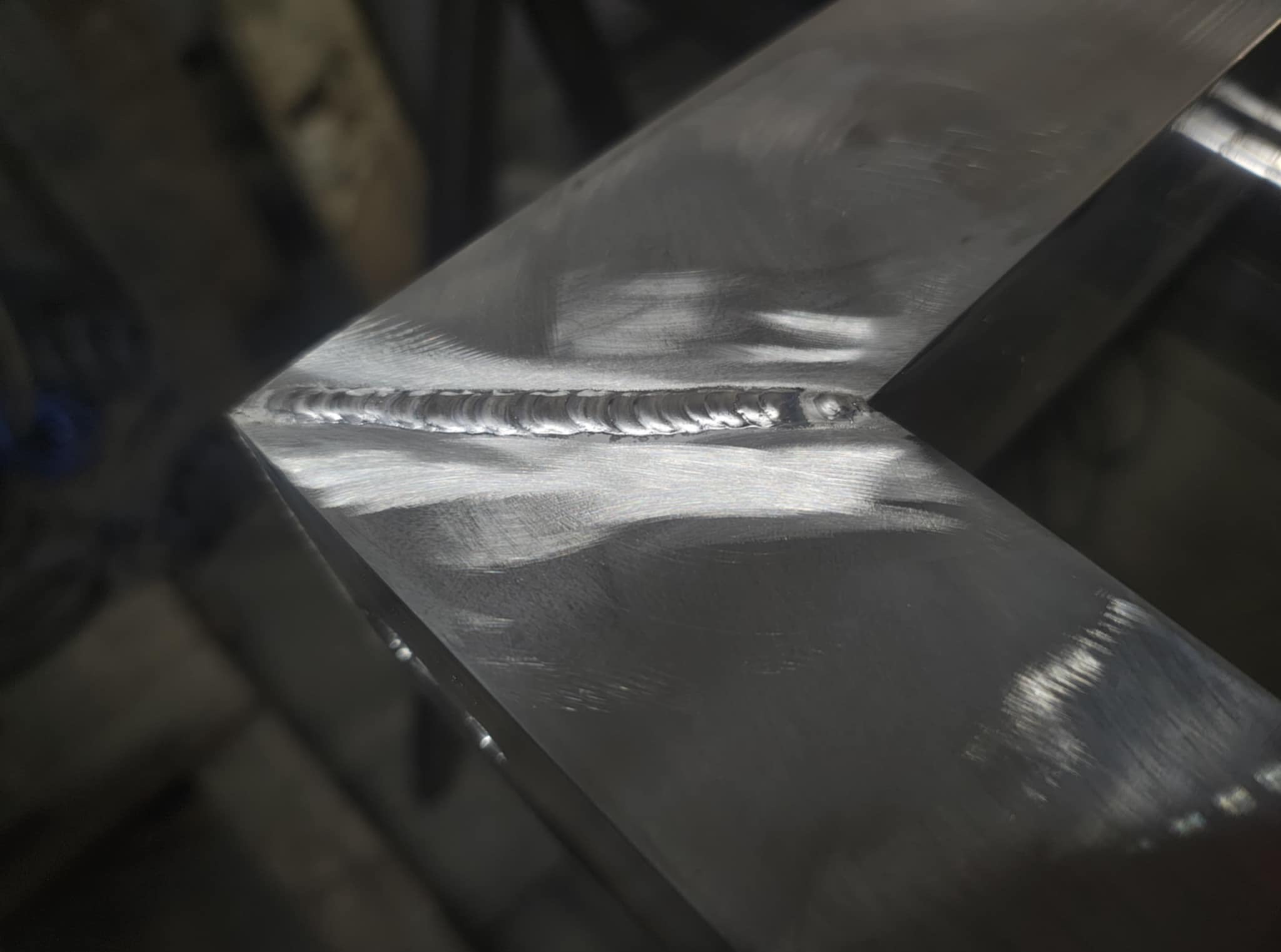 Szczegółowe zbliżenie na spawany narożnik metalowej konstrukcji. Widoczny równy, estetyczny spaw na szlifowanej powierzchni. Precyzyjne łączenie elementów.