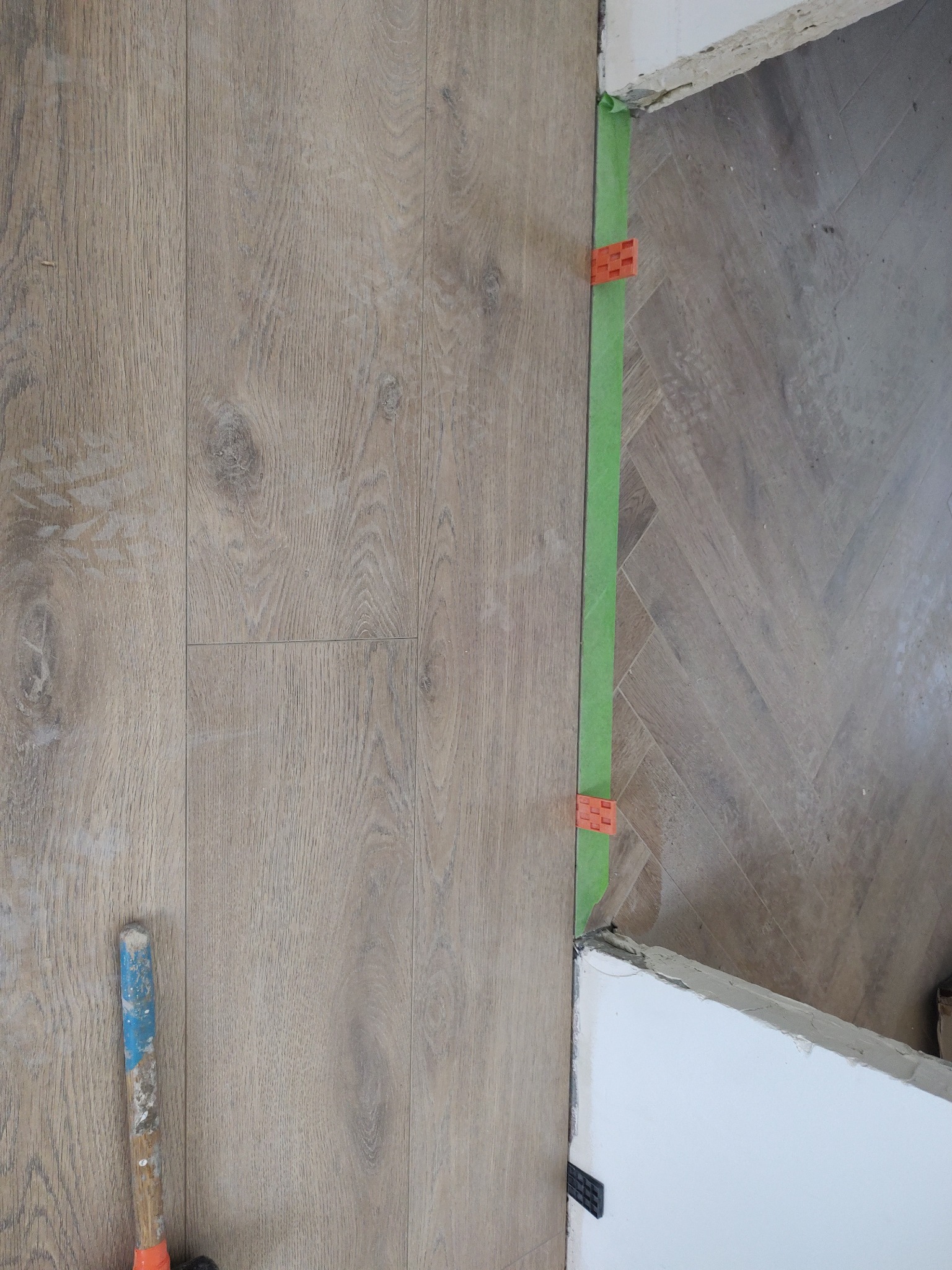 Układanie paneli podłogowych z użyciem poziomicy i klipsów dystansowych; widoczny fragment młotka.