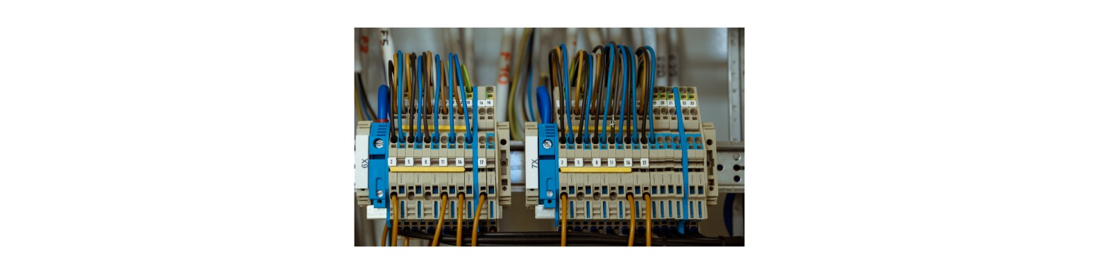 Dwa panele elektryczne z kolorowymi przewodami podłączonymi do listew zaciskowych, widoczne numery identyfikacyjne przewodów.