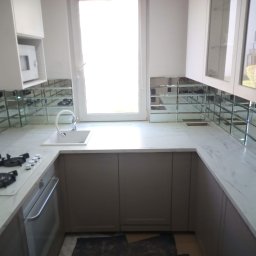 A.D.G - Nowoczesna kuchnia z białymi szafkami, marmurowym blatem i lustrzaną mozaiką na ścianie, widok na okno i zabudowany piekarnik.