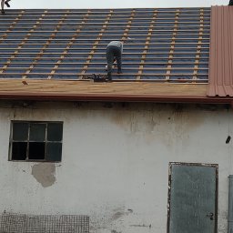 Eko - Dach - Prace na dachu budynku gospodarczego: układanie łat pod pokrycie dachowe, widoczna stara, zniszczona elewacja i okno.