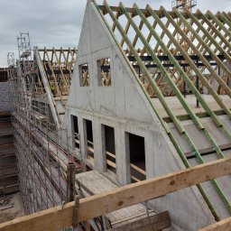 Eko - Dach - Konstrukcja dachu z betonu i drewna na budynku w trakcie budowy, widoczne rusztowania i dźwig w tle, pochmurne niebo.