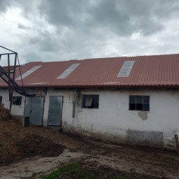 Eko - Dach - Budynek gospodarczy z nowym, brązowym dachem z trzema świetlikami, widoczny stary podajnik do siana i sterta siana na pierwszym planie.