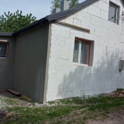 Eko - Dach - Dom w trakcie ocieplania elewacji styropianem, z widocznym fragmentem otynkowanej dobudówki, okna zabezpieczone folią, na trawie resztki styropianu.