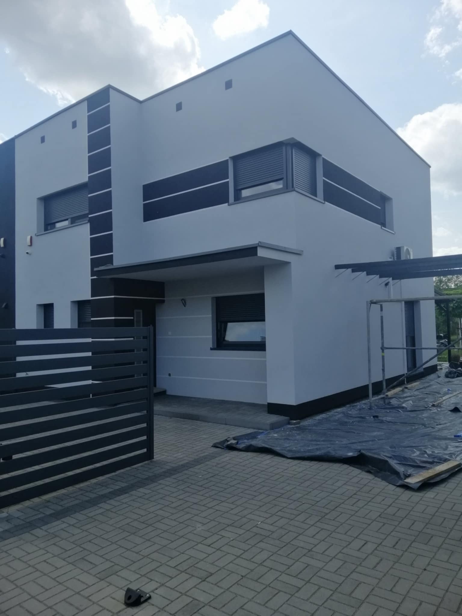 Nowoczesny dom po malowaniu elewacji w odcieniach szarości z czarnymi akcentami. Widoczne rusztowania i zabezpieczenia, sugerujące świeżo zakończone prace.