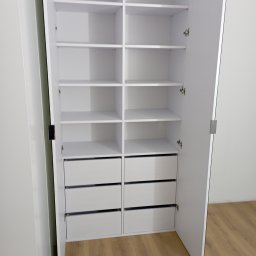 Tomasz Kuna Strefa Mebli - Biała szafa wnękowa z otwartymi drzwiami, widoczne półki i szuflady, minimalistyczny design, jasne wnętrze, drewniana podłoga.