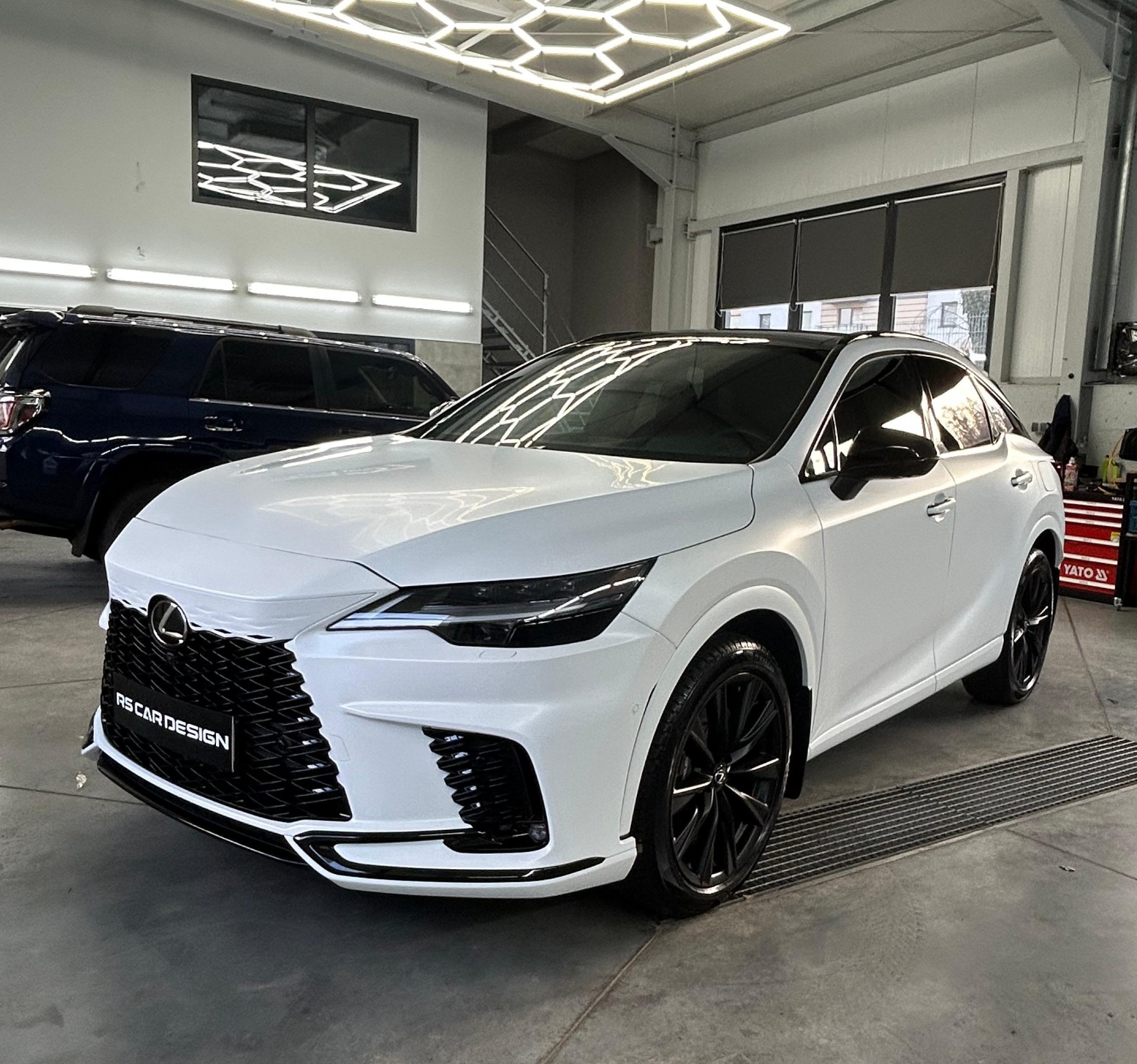 Biały Lexus RX z czarnymi akcentami po detailingu w warsztacie. Widoczne logo RS Car Design na grillu i narzędzia YATO w tle. Nowoczesne oświetlenie sufitowe.