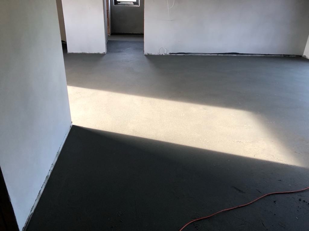 Świeżo wylana, gładka posadzka w surowym wnętrzu z widocznym promieniem słonecznym i fragmentem czerwonego kabla.