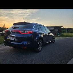 Jakub Pakulski - Granatowy samochód kombi Renault Megane, zaparkowany na asfalcie, widok z tyłu, w tle zachód słońca i budynek gospodarczy.