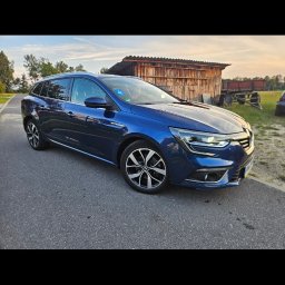 Jakub Pakulski - Niebieski samochód kombi marki Renault zaparkowany na asfaltowej drodze, z widocznym budynkiem gospodarczym w tle.