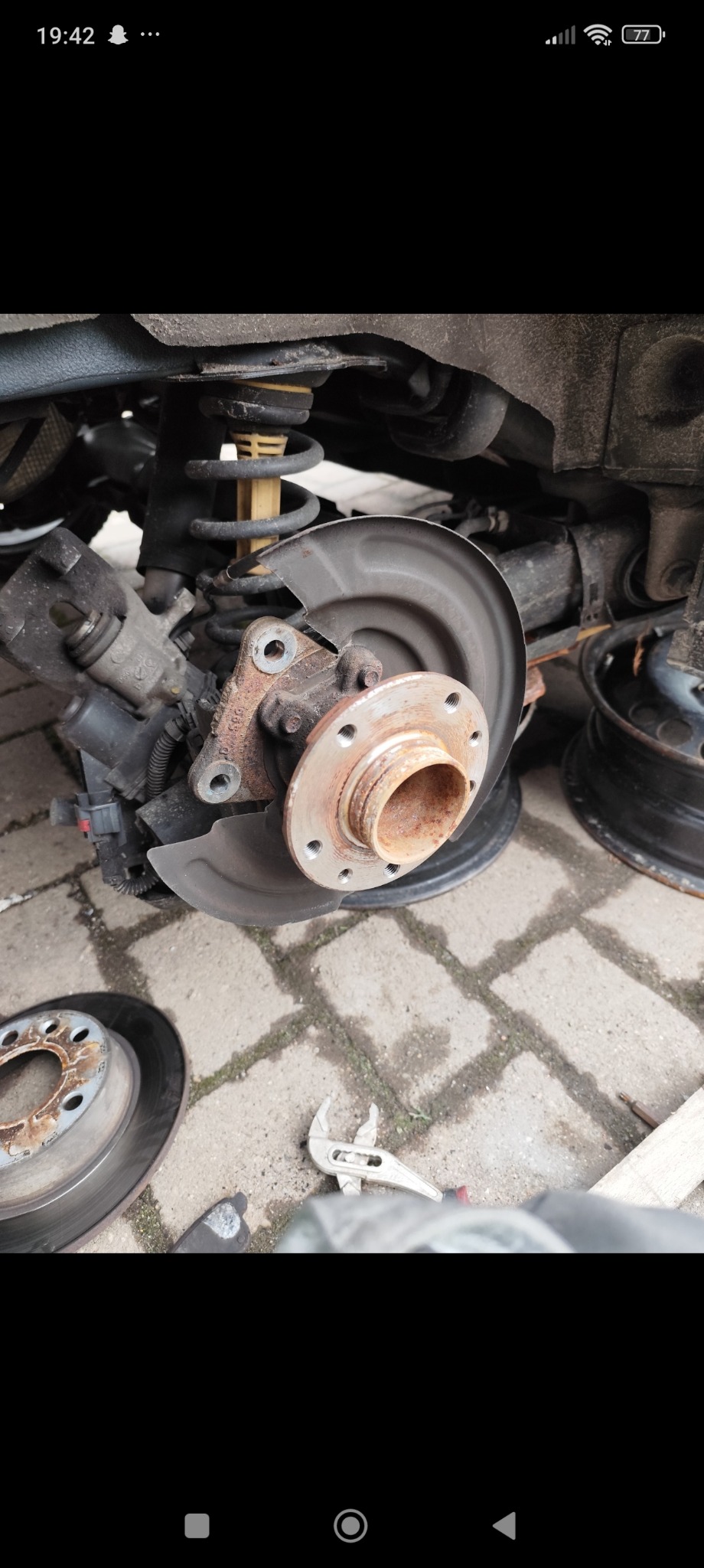 Zawieszenie samochodu z widoczną sprężyną i tarczą hamulcową, obok leżąca tarcza hamulcowa i klucz nastawny.