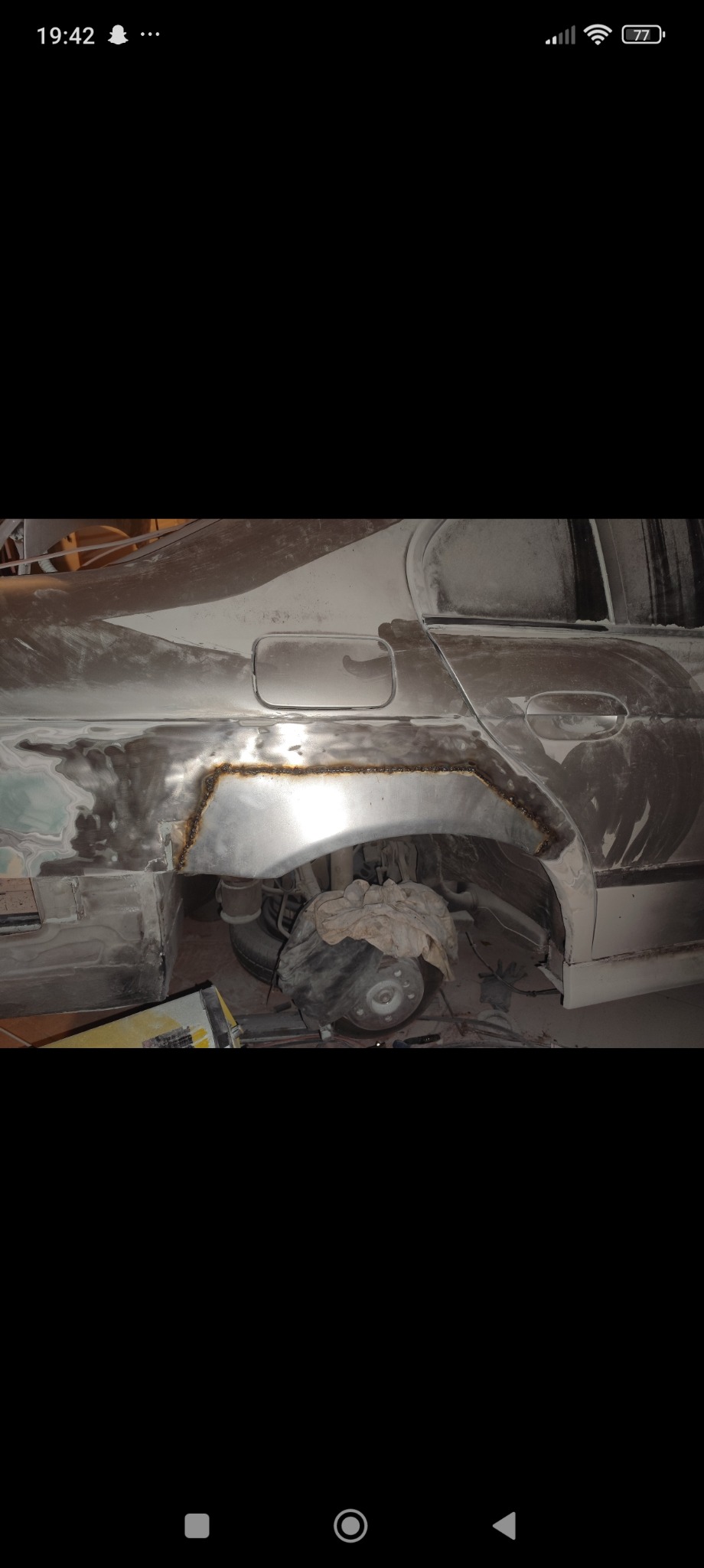 Fragment samochodu w trakcie naprawy blacharskiej, widoczne ślady spawania na nadkolu, szpachla i przygotowanie do lakierowania.