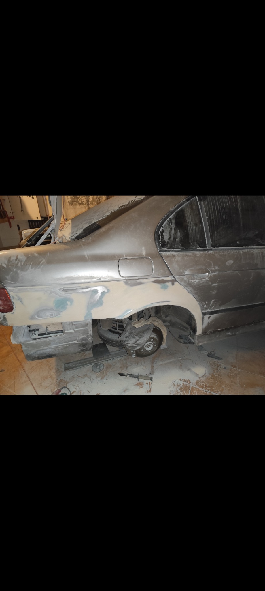 Przygotowanie karoserii do lakierowania w Kruszynie: szlifowanie i nakładanie szpachli na tylnym błotniku samochodu osobowego.