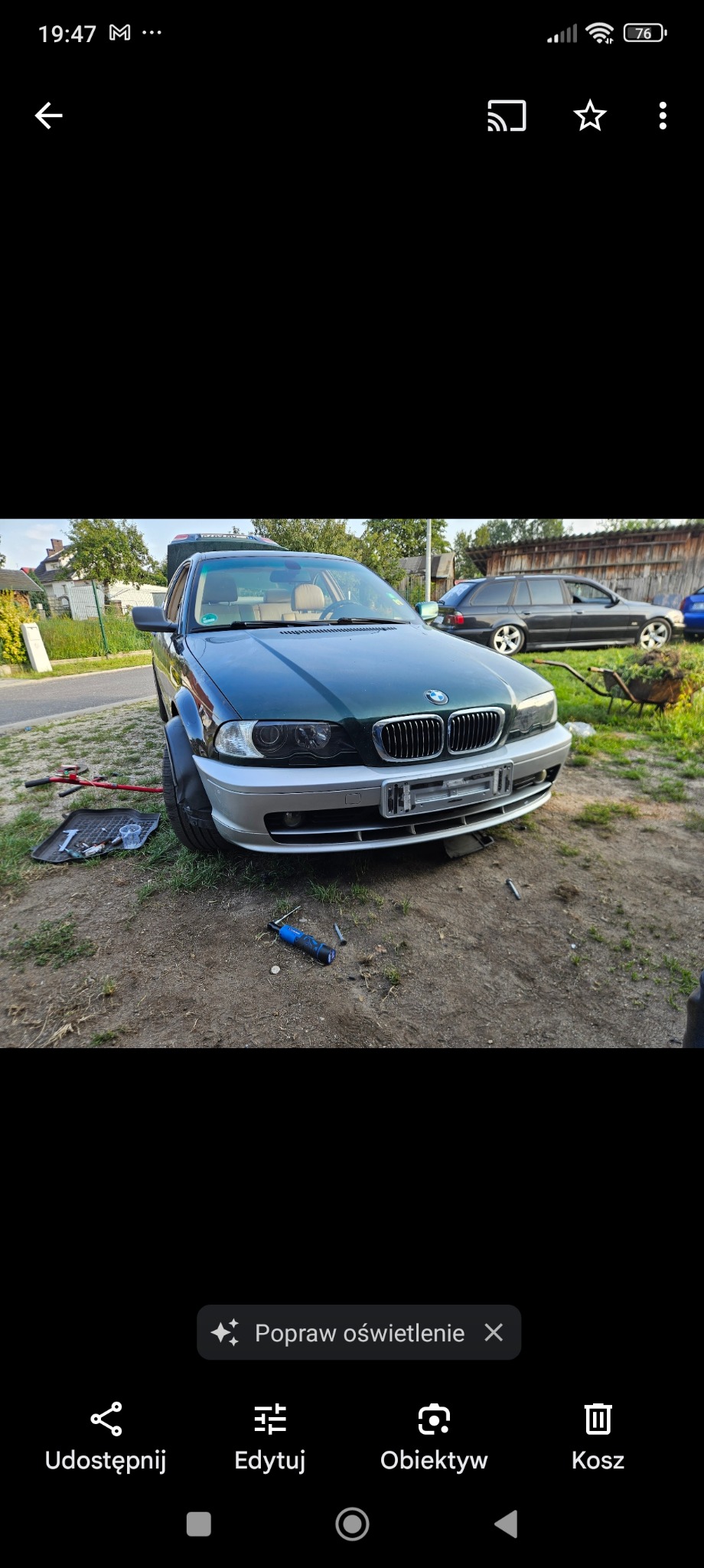 Zielony samochód BMW serii 3 z srebrnym zderzakiem w trakcie naprawy na zewnątrz, widoczne narzędzia i podnośnik.