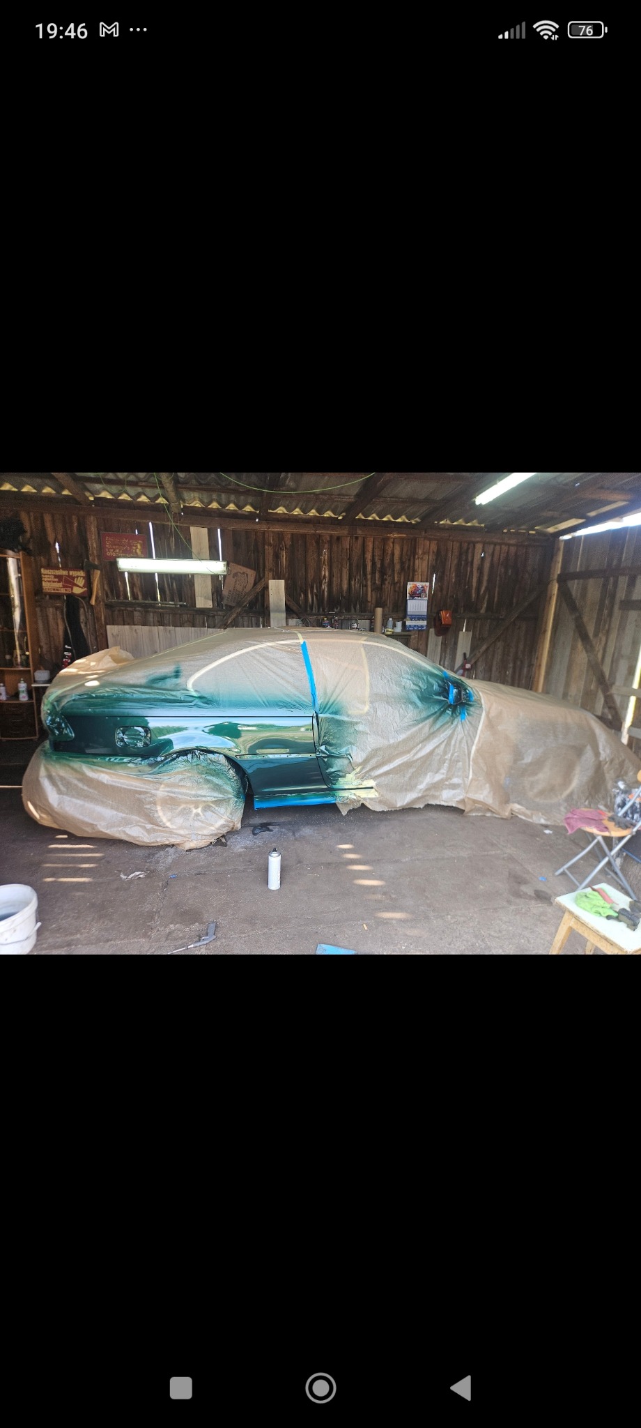 Samochód częściowo oklejony folią ochronną i taśmą maskującą, w trakcie malowania na zielono w garażu z drewnianymi ścianami, widoczna puszka z farbą w sprayu.