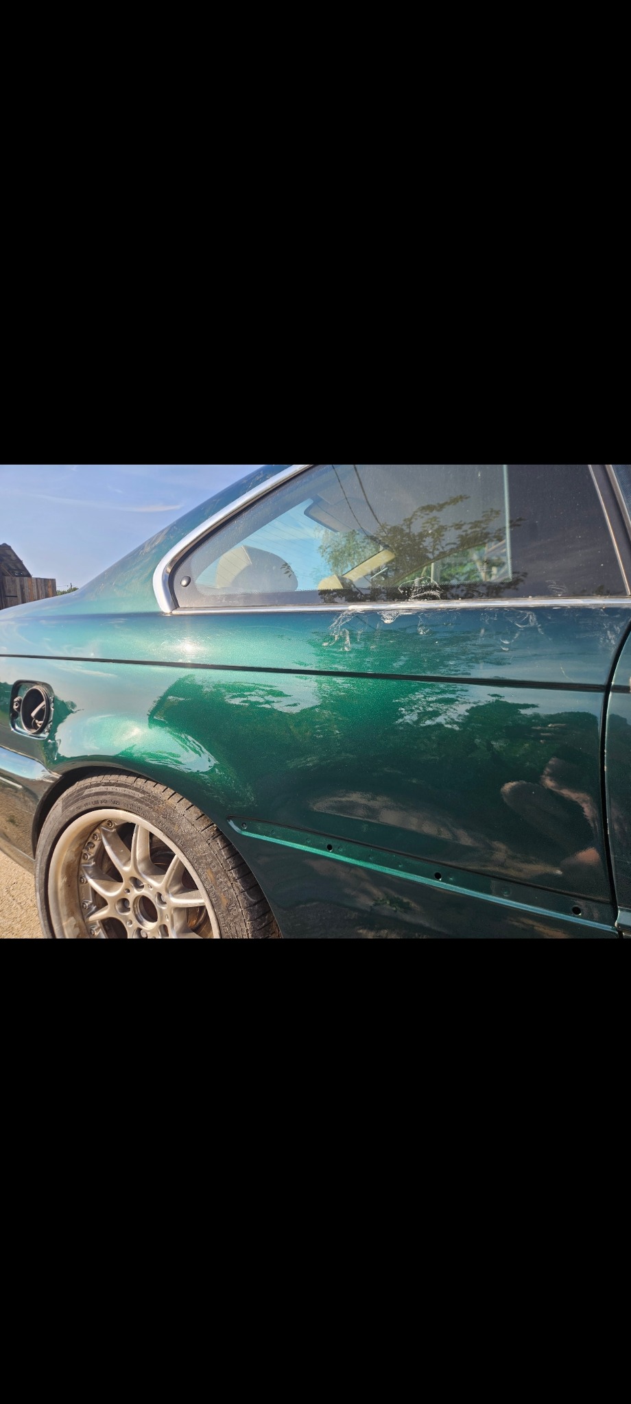 Uszkodzony, zielony samochód z widocznymi zarysowaniami i brakiem listwy bocznej, ukazujący potrzebę napraw blacharsko-lakierniczych.