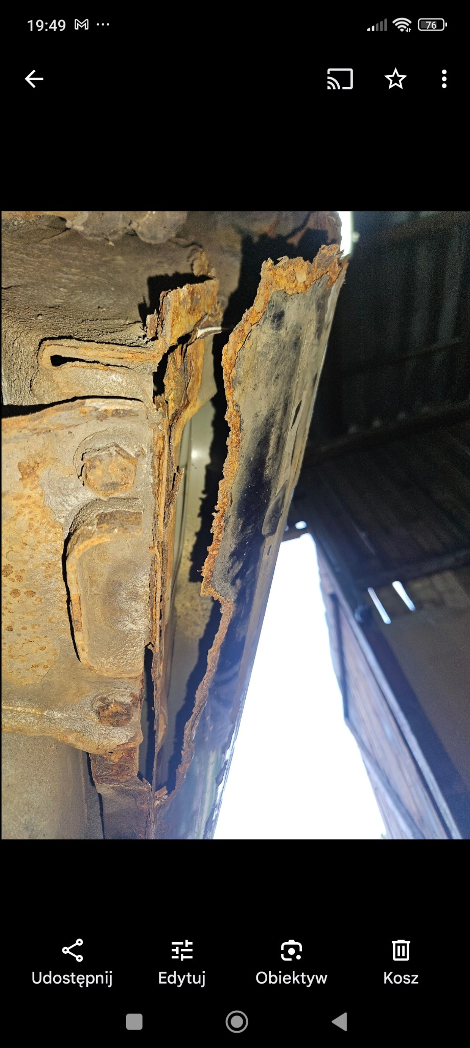 Silnie skorodowany próg samochodu, widoczne liczne ogniska rdzy i ubytki metalu, sfotografowane od dołu z perspektywy osoby leżącej pod pojazdem.