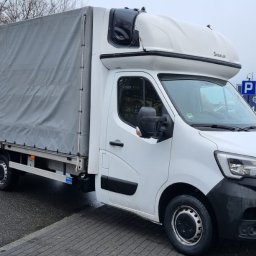 MAT-TRANS MATEUSZ ŚWIDERSKI - Biały samochód dostawczy Renault Master z wysoką kabiną i plandeką, zaparkowany na parkingu, z widocznym billboardem reklamowym w tle.