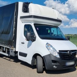 MAT-TRANS MATEUSZ ŚWIDERSKI - Biały samochód dostawczy z plandeką marki Opel Master, zaparkowany na asfaltowej drodze z widokiem na zielone pola i błękitne niebo z chmurami.