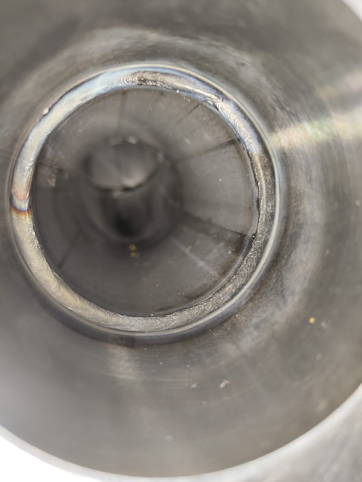 Wnętrze metalowej rury z widocznym spoiwem po spawaniu obwodowym, z lekkimi przebarwieniami termicznymi i drobnymi zanieczyszczeniami.