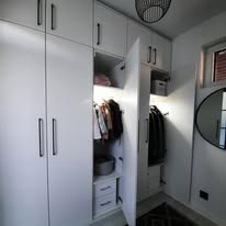 Biała szafa wnękowa z otwartymi drzwiami, czarne uchwyty, okrągłe lustro na ścianie, widok z dołu, oświetlenie wewnętrzne szafy.