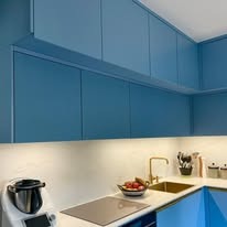 Niebieska zabudowa kuchenna z górnymi szafkami, złota bateria i oświetlenie LED pod szafkami, nowoczesny robot kuchenny na blacie.