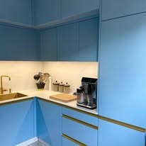 Błękitna kuchnia z blatem z jasnego marmuru, złota armatura i ekspres do kawy. Ujęcie z boku, widoczny fragment szafek górnych.