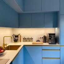 Niebieska kuchnia na wymiar z złotymi akcentami: zlew, bateria i uchwyty. Nad blatem szafki podświetlone ledami. Na blacie ekspres do kawy i akcesoria kuchenne.