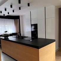 Nowoczesna kuchnia: wyspa z drewnianym frontem i czarnym blatem, białe szafki, oświetlenie punktowe. Minimalistyczny design z elementami naturalnego drewna.