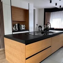 Nowoczesna kuchnia: drewniane fronty dolnych szafek, czarny blat, białe górne szafki z drewnianymi wnękami. Widoczny ekspres do kawy i inne akcesoria.