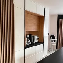 Biała kuchnia na wymiar z drewnianymi akcentami: ryflowane panele na szafce, drewniana wnęka z ekspresem do kawy. Nowoczesny design, oświetlenie punktowe.