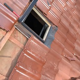 Davi-Bau - Montaż okna dachowego w pokryciu z dachówki ceramicznej w odcieniach brązu. Widoczny fragment dachu z narzędziem pracy - młotkiem dekarskim.