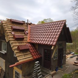 Davi-Bau - Częściowo pokryty dach domu brązową dachówką ceramiczną. Widoczne drewniane łaty i membrana dachowa. Część dachu jeszcze przed położeniem dachówki.