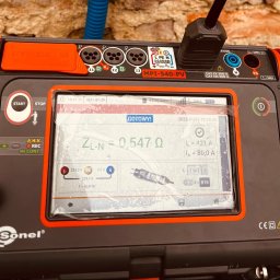 VARTECH RAFAŁ KASPRZAK - Miernik Sonel MPI-540-PV z wyświetlonym wynikiem pomiaru impedancji pętli zwarcia ZL-N = 0,547 Ω, wykonany na tle ceglanej ściany.