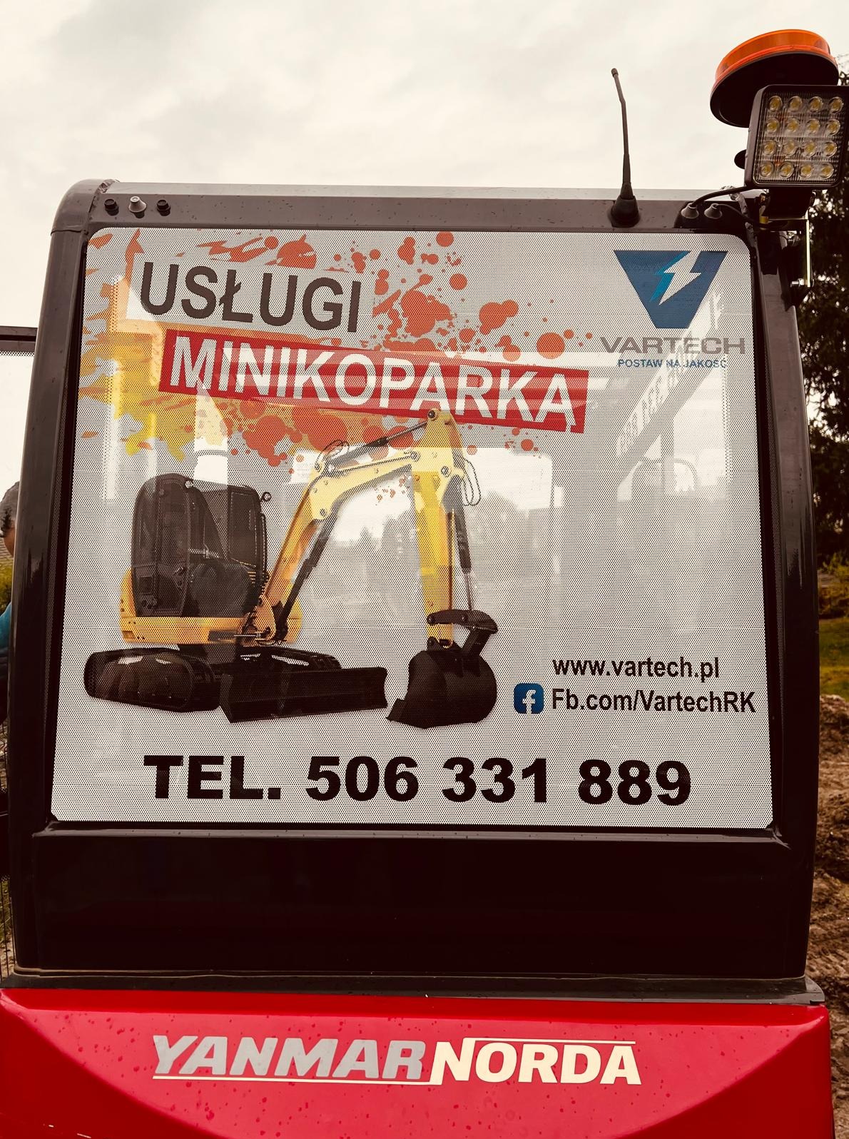 Grafika na tylnej szybie minikoparki Yanmar Norda z reklamą usług minikoparką firmy Vartech, numer telefonu i adres strony internetowej.
