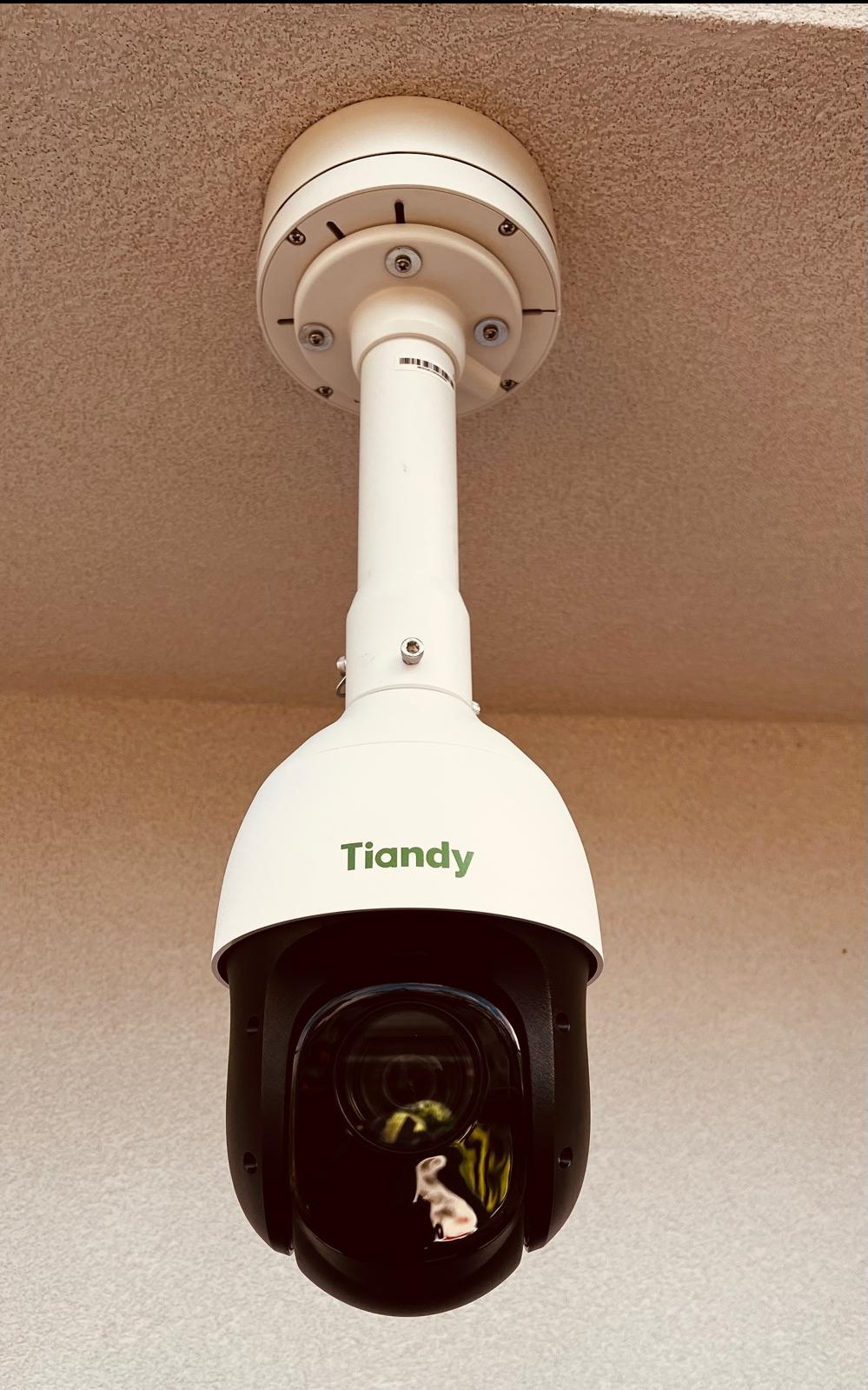 Kamera monitoringu Tiandy zamontowana na suficie, widoczna tekstura sufitu i ściany, odbicie w obiektywie.