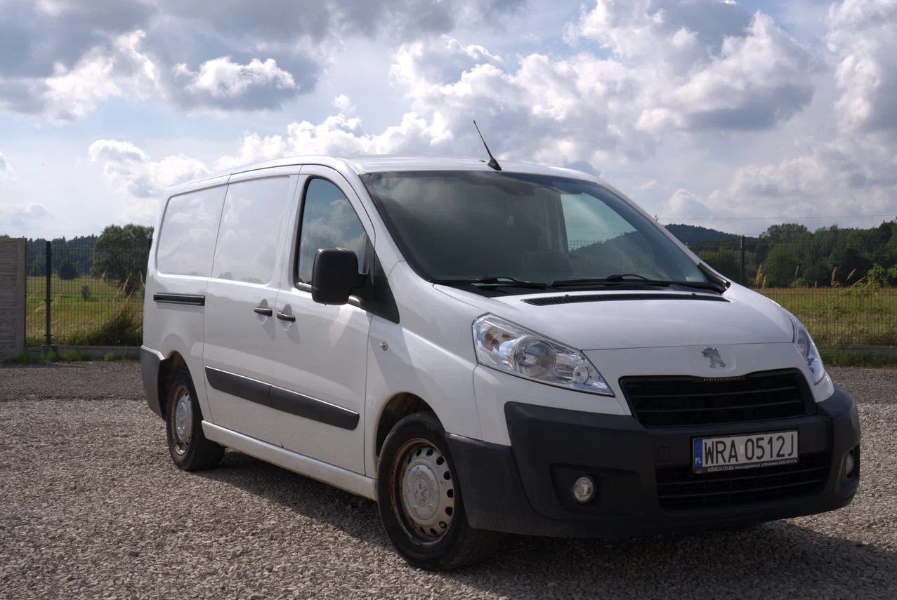 Biały samochód dostawczy Peugeot Expert zaparkowany na żwirowym placu, z widoczną tablicą rejestracyjną i anteną na dachu.