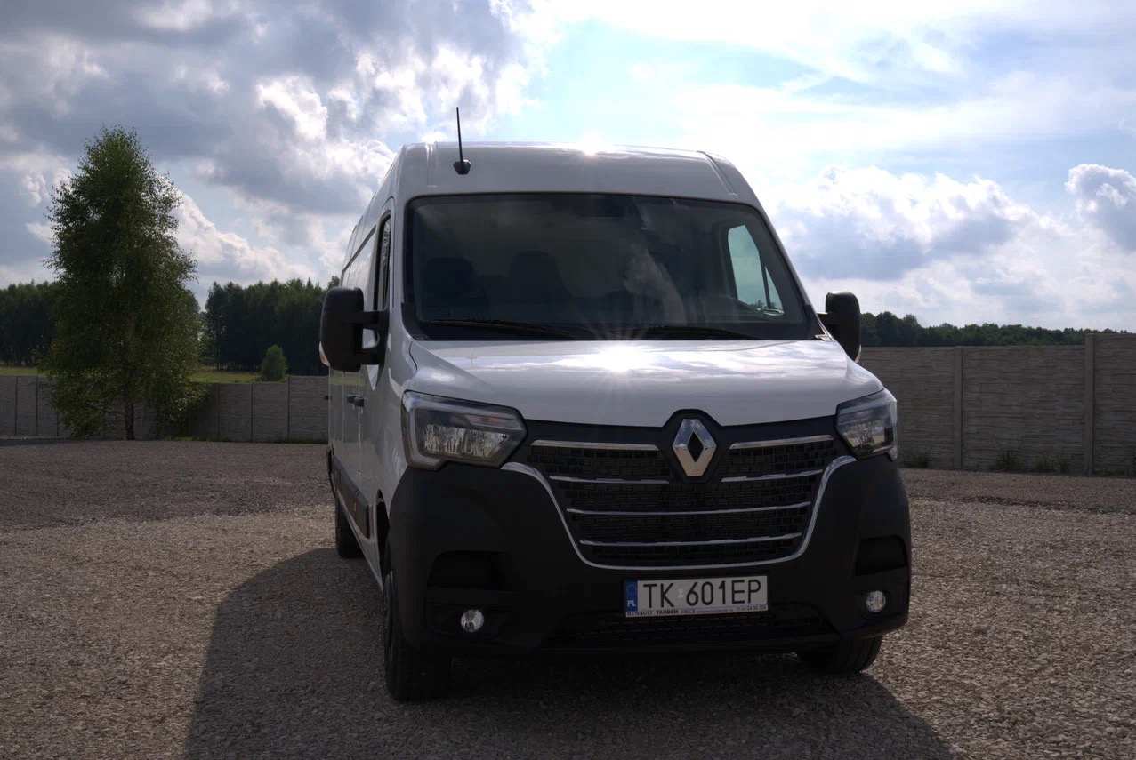 Biały Renault Master z anteną na dachu, zaparkowany na żwirowym placu, z widoczną tablicą rejestracyjną TK 601EP i drzewem w tle.