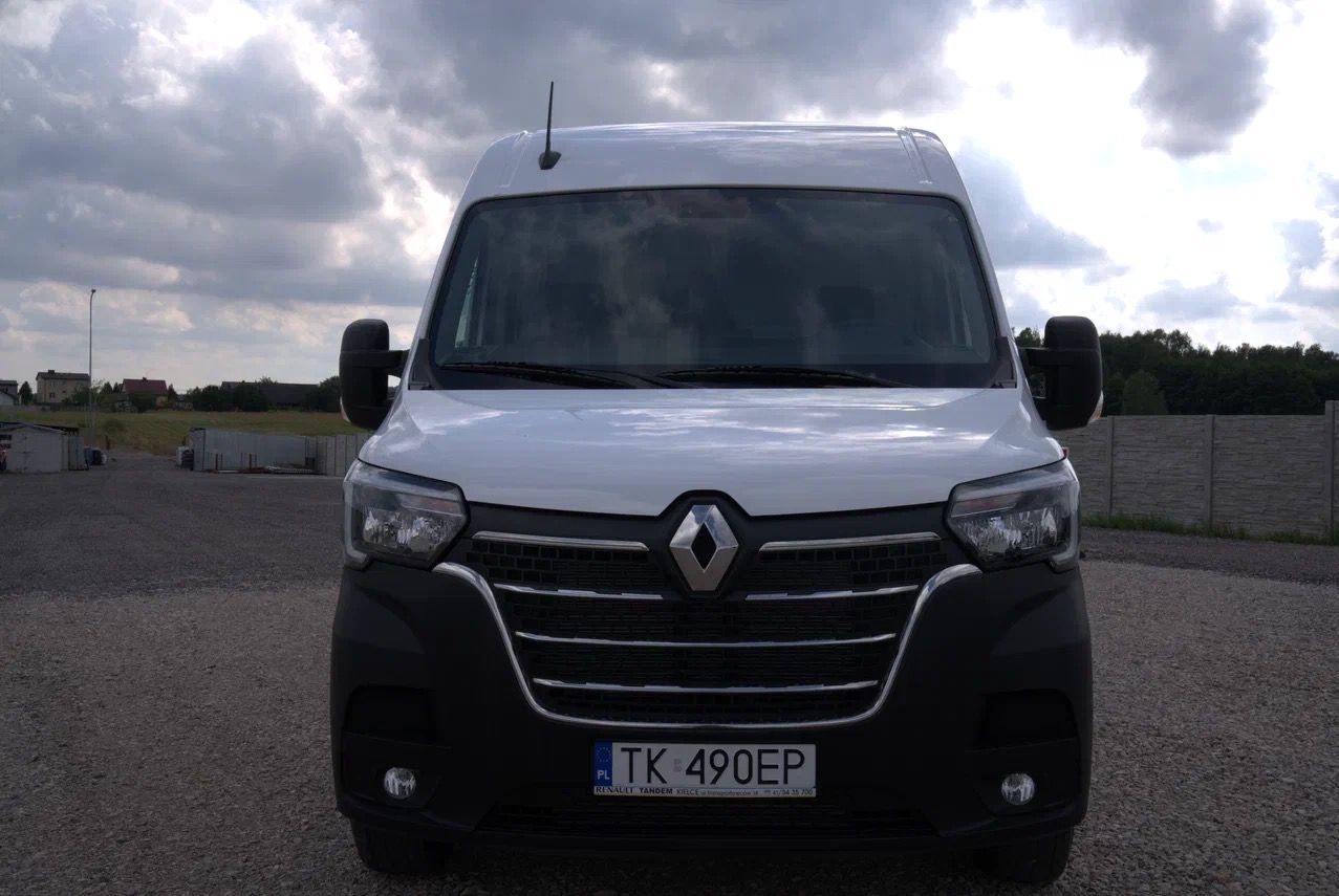 Przód białego samochodu dostawczego Renault Master z widoczną tablicą rejestracyjną na tle pochmurnego nieba.