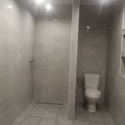 WOJCIECH MAMAK - Wykończona łazienka z szarą glazurą, kabiną prysznicową typu walk-in i toaletą kompaktową, oświetlona punktowymi lampami sufitowymi.