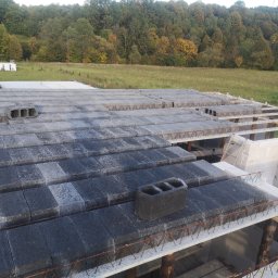 WOJCIECH MAMAK - Wznoszenie stropu Teriva na budowie w Hoczewiu, widoczne pustaki stropowe i zbrojenie, w tle zielone drzewa.